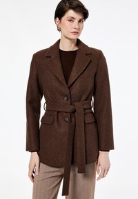 Blazer marrón de mezcla de lana con cintura ceñida con cinturón, solapas con muesca y dos bolsillos frontales. Presenta botones negros y un acabado texturizado.