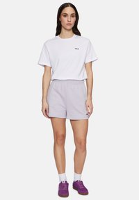 T-shirt bianca in cotone con logo "FILA" nero, abbinata a pantaloni corti viola chiaro e sneakers viola, con calzini bianchi alla caviglia.