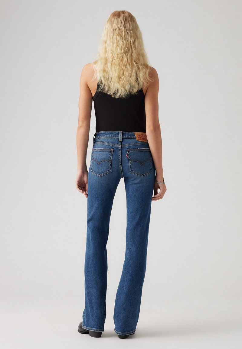 Jeans évasés en denim bleu clair à taille haute, dotés de poches arrière avec des détails de couture et d'une étiquette en cuir sur la ceinture.