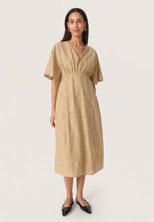 Beige bomulds midi kjole med V-udskæring, korte flæseærmer og diamantudskæringsmønster. Bæres med sorte spidse flade sko.