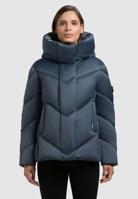 Tumesinine polsterdatud jope kõrge kraega, diagonaalse tikandmustriga, küljetaskute ja tekstuurse viimistlusega. Disainitud soojuse tagamiseks.