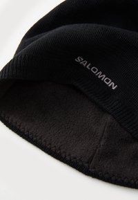 Čierna čiapka s ryhovaným pletením, s mäkkou čiernou fleecovou podšívkou. Na prednej strane vyšitý biely logo "SALOMON".