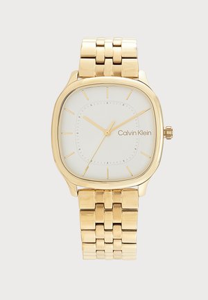 Złocony metalowy zegarek na rękę z kwadratową białą tarczą, minimalistycznymi złotymi znacznikami godzin, trzema wskazówkami i logo Calvin Klein na tarczy.