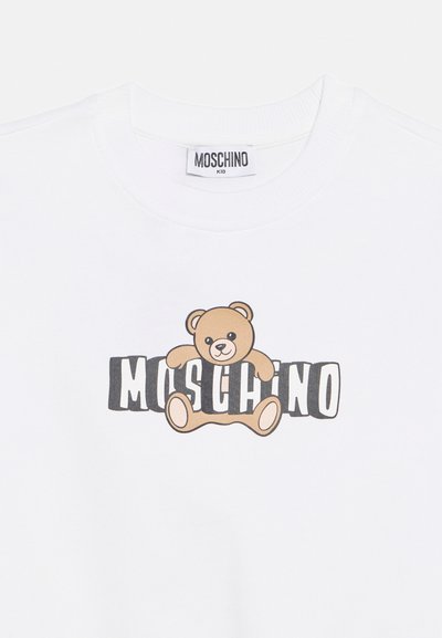 Hvit barne-T-skjorte med en teddybjørngrafikk som holder rundt ordet "MOSCHINO" skrevet med fete svarte og hvite bokstaver.