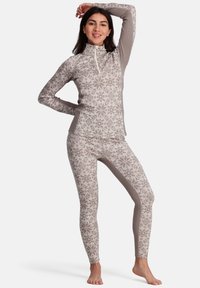 Langsleeve, hoge hals top en strakke legging in lichtbeige met een subtiel geometrisch patroon. De stof lijkt zacht en textuur te hebben.