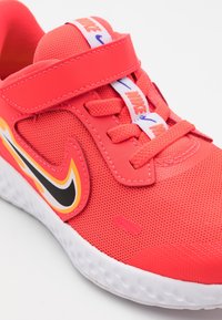 Červená síťovaná sportovní obuv s černými a oranžovými akcenty, vybavená širokým suchým zipem a texturovanou bílou gumovou podrážkou.