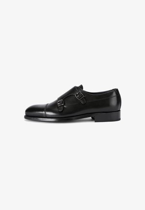 Chaussure habillée en cuir noir avec un design élégant, bout rond, accents à double boucle et un petit talon. Texture lisse et finition polie.
