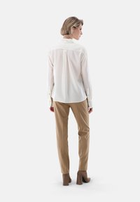 White, long-sleeve shirt with a structured collar, paired with tan, slim-fit pants. Material appears smooth; pants feature a subtle texture.