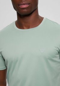 Camiseta de manga corta verde claro con escote redondo y tejido texturizado. Presenta un pequeño logo triangular en relieve en el pecho.