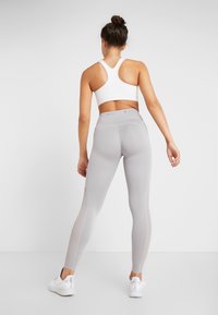 Szare legginsy z wysokim stanem, z bezszwową konstrukcją, teksturowanymi panelami i białym stanikiem sportowym. Oba wykonane z rozciągliwego materiału.