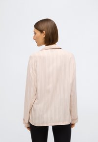 Cămașă roz deschis cu guler, cu dungi verticale, mâneci lungi și croială lejeră. Textură fină și luciu subtil. Design simplu, fără accente notabile.