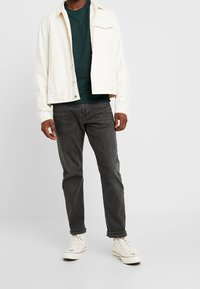 White denim jacket over a green sweatshirt, paired with gray jeans and white high-top sneakers. Casual design with simple lines.