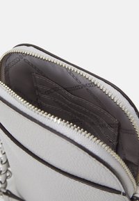 Borsa a spalla in pelle bianca testurizzata con una cerniera metallica, presenta un interno beige e slot per carte. Catena a tracolla visibile.