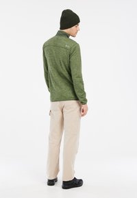 Groene textuur lange mouw top met een hoge kraag, gecombineerd met beige cargo broek en zwarte schoenen, met een getailleerd ontwerp en subtiele logodetails.