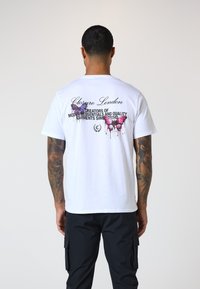 Weißes Baumwoll-T-Shirt mit buntem Schmetterlingsdruck und Text auf der Rückseite, kombiniert mit schwarzen Cargo-Hosen. Schlichtes und lässiges Design.