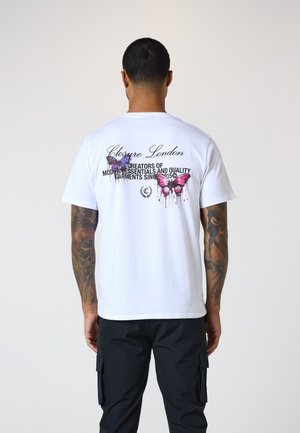 Weißes Baumwoll-T-Shirt mit buntem Schmetterlingsdruck und Text auf der Rückseite, kombiniert mit schwarzen Cargo-Hosen. Schlichtes und lässiges Design.