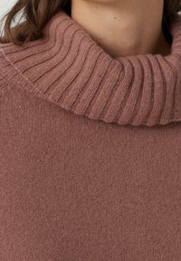 Vaaleanpunainen ribbineuleinen pooloneule, jossa on pehmeä tekstuuri. Kauluksessa on paksu ribbineule ja vartalo on sileä ja istuva.