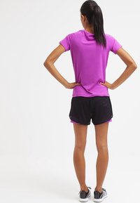 Lila kurzärmeliges Sportoberteil mit glatter Textur, kombiniert mit schwarzen, leichten Shorts mit geschichtetem Design und atmungsaktivem Stoff.