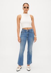 Valkoinen ribbed cropped-top, jossa on aallotettu helma, yhdistettynä vaaleansinihin laahushousuihin. Asusteina beige aurinkolasit ja valkoiset kengät.