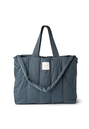 Sac cabas matelassé bleu foncé avec deux poignées courtes et une longue bandoulière, doté d'une étiquette blanche centrée sur le devant.