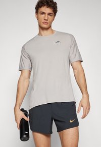 Light gray athletic t-shirt with short sleeves and a small logo; paired with dark shorts featuring side pockets and a Nike logo. Black water bottle.