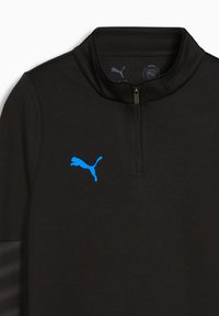 Juodas megztinis su aukštu apykaklės, su mėlynu Puma logotipu. Pagamintas iš tekstūruoto audinio, priekioje turi pusę užtrauktuko.
