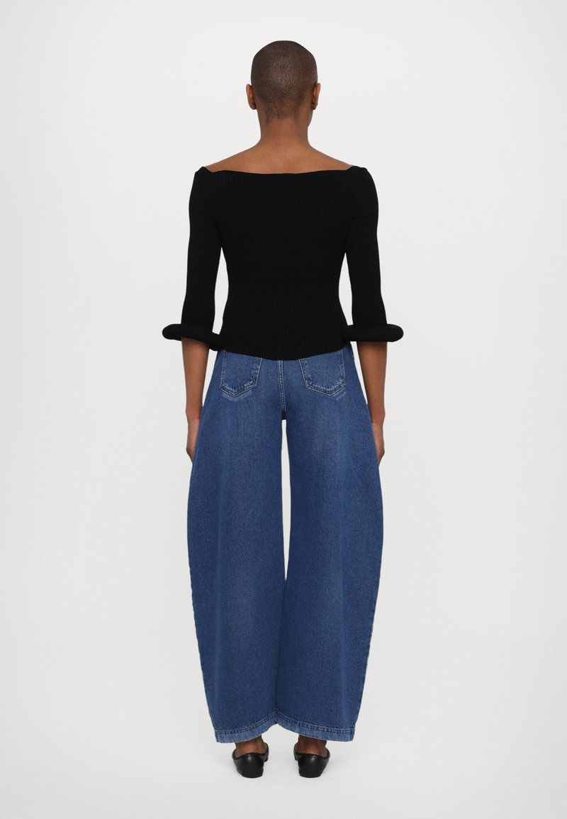 Black ribbed off-shoulder top with three-quarter sleeves paired with wide-leg blue denim jeans, featuring a high waist and back pockets.