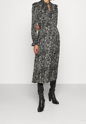Kvinde iført en sort og hvid paisley midi kjole med lange ærmer og sorte knæhøje støvler med hæl.
