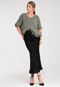 Gruba, oliwkowa dzianinowa bluzka z krótkim rękawem w połączeniu z czarną satynową spódnicą maxi, charakteryzującą się luźnym krojem i gładką teksturą.