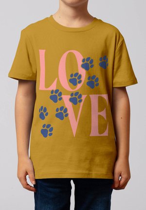 Enfant portant un T-shirt jaune moutarde avec le texte rose "LOVE" et plusieurs empreintes de pattes bleues dispersées sur le devant.