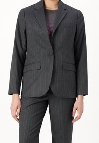 Grå randig blazer med skräddarsydd design, urklippta slag, enkel knappstängning och två framfickor. Bärs över en grå skjorta.