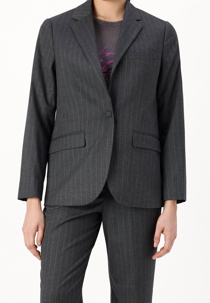 Grå randig blazer med skräddarsydd design, urklippta slag, enkel knappstängning och två framfickor. Bärs över en grå skjorta.