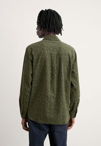 Camicia verde stampata con colletto a bottone, maniche lunghe e spacco sul retro. Il motivo presenta piccoli puntini bianchi e blu sul tessuto.
