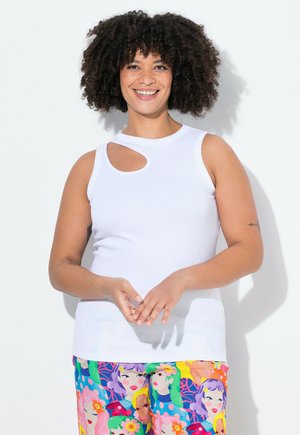 Haut blanc sans manches avec un col arrondi et une découpe sur le côté. Le modèle porte un pantalon à motifs colorés avec des visages graphiques et des couleurs vives.