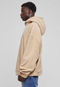 Beige hoodie met een losse pasvorm en geribbelde manchetten, gemaakt van zacht materiaal. Heeft een kangoeroezak aan de voorkant.