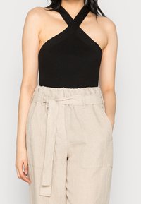 Top nero a coste con collo allacciato al collo e spalline incrociate, abbinato a pantaloni beige a vita alta con cintura annodata e tasche laterali.