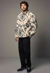 Fleece pullover i creme med sorte udsmykninger, høj krave og elastiske manchetter. Sammen med sorte bukser og sorte sneakers.