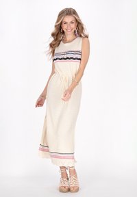 Rochie maxi din tricot crem cu talie ajustabilă, având dungi orizontale multicolore și detalii cu margini ondulate. Purtați cu sandale cu curea.