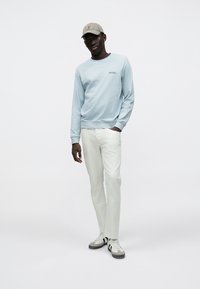 Ανοιχτό μπλε φούτερ με μακριά μανίκια και στρογγυλή λαιμόκοψη. Λευκό παντελόνι και ανοιχτό γκρι αθλητικά παπούτσια με μαύρες λεπτομέρειες. Μπεζ καπέλο ολοκληρώνει την εμφάνιση.