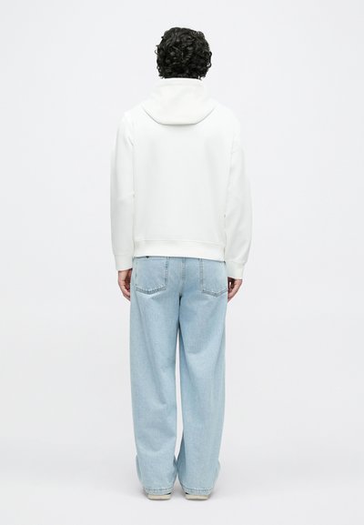 Baltas džemperis su raišteliu gobtuvu, derinamas su šviesiai mėlynomis, plačiomis kelnėmis. Lygus audinys be pastebimų raštų ar detalių.