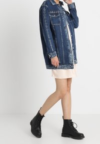 Jeansová bunda v tmavě modré barvě s náprsními kapsami, stříbrnými přezkami a zapínáním na knoflíky. Nositá přes lehké šaty, doplněná černými šněrovacími botami.