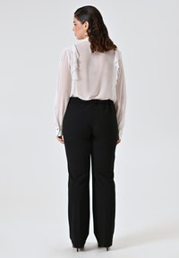 Blusa bianca con dettagli a volant, abbinata a pantaloni neri. La blusa presenta maniche lunghe e un collo rotondo, mentre i pantaloni hanno una vestibilità comoda.