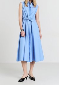 Jasnoniebieska, bezrękawnikowa sukienka koszulowa z zapinaniem na guziki z przodu i wiązanym paskiem w talii. Luźna spódnica sięga do połowy łydki. Noszona z czarnymi, na wysokim obcasie klapkami.