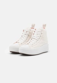 Pár vysokých tenisek s bílými tkaničkami, silnými bílými podrážkami a krémovými texturovanými fleecovými svršky na jednobarevném pozadí.