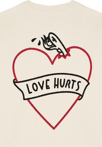 Maglione di cotone crema con una grafica di un cuore rosso trafitto da un coltello nero. Un banner sottostante riporta la scritta "LOVE HURTS" in lettere grasse.