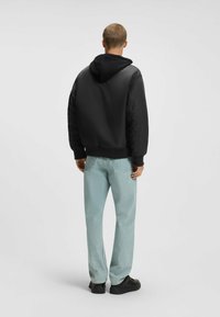 Veste bomber noire à capuche avec une finition lisse et des manches bouffantes, associée à un jean droit bleu clair et des baskets noires.