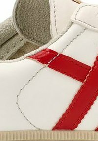 Zapato de cuero blanco con una franja diagonal roja, detalles de costura y un forro interior texturizado. Utiliza una correa de velcro para el cierre.