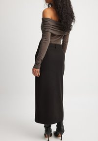 Off-shoulder, mauve top med samlede stof; parret med en tætsiddende sort nederdel og højhælede sorte støvler. Glatte teksturer og minimale detaljer.