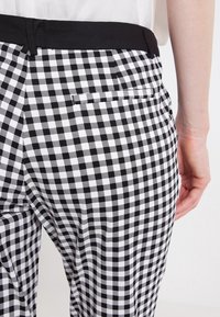 Pantalons en vichy noir et blanc avec une texture lisse, taille ajustée et une poche arrière visible sur le côté droit.