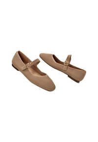 Zapatos Mary Jane en tono marrón claro con parte superior de tela acanalada, suela plana y correa ajustable con un hebilla rectangular. Punta redondeada.